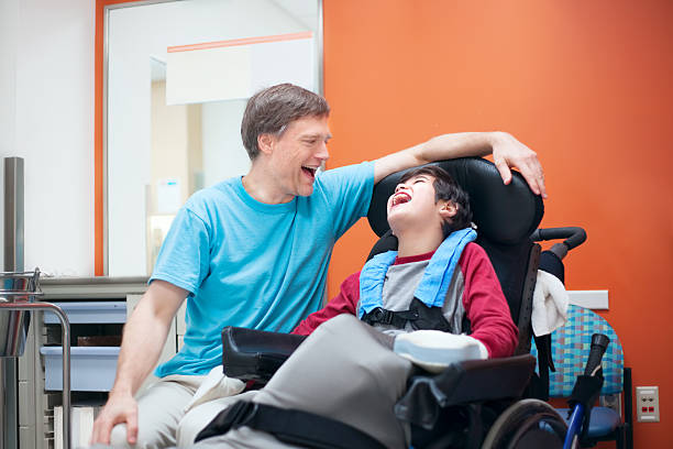 Bambino disabile in sedia a rotelle che parla con il padre in camera d'ospedale - foto stock