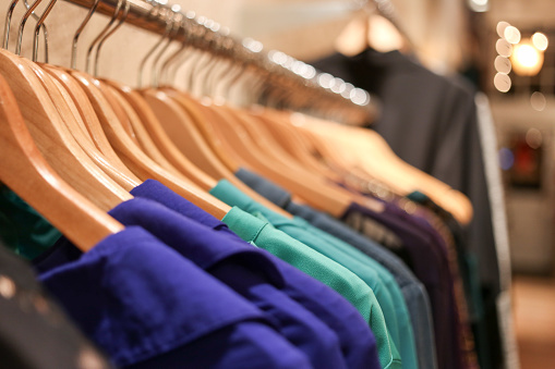 Several cool colored shirts hang on wooden hangers across a rack.