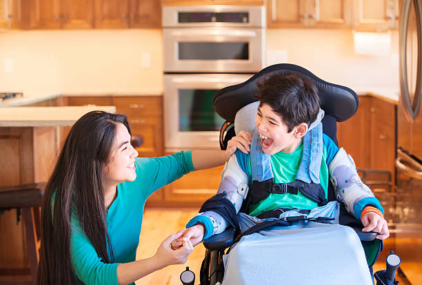 Ragazzo disabile in sedia a rotelle ridendo con sorella adolescente in cucina - foto stock