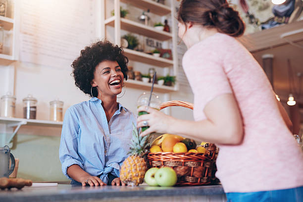 Juice bar owner talking to female customer Portrait of young african woman standing behind juice bar counter and talking with female customer holding a glass of fresh juice. juice bar stock pictures, royalty-free photos & images