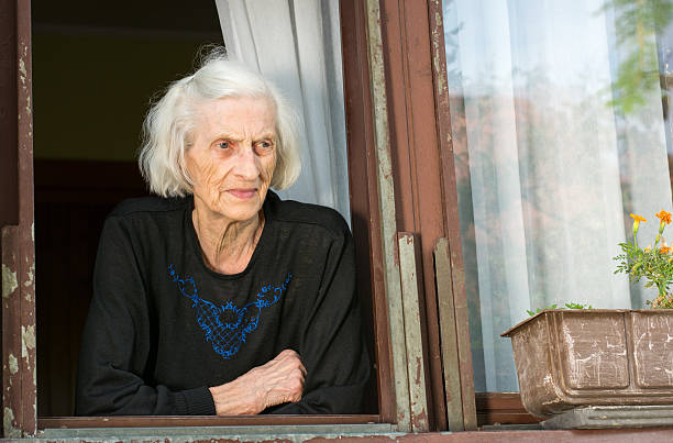 istock Senior woman alone on house window 580116098