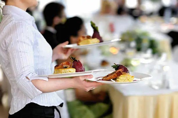 Waitress carrying three plates with meat dish