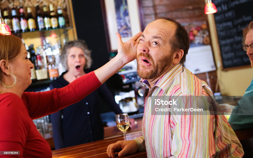 Woman Slaps Funny Man in Bar Woman slaps a man in a bar, while another woman looks on with a shocked expression. Some humor involved! Slapping Stock Photo