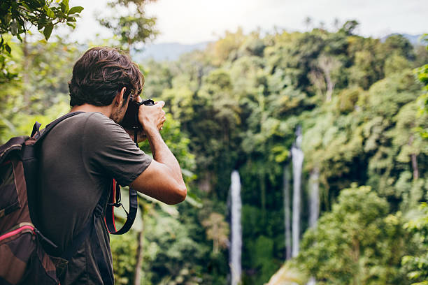 male hiker photographing a waterfall in forest - nature travel locations imagens e fotografias de stock