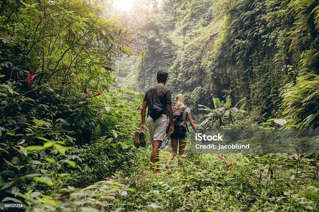 Young couple walking through woods Rear view of young couple walking through woods with their shoes in hand. Man and woman hiking in forest. Rainforest Stock Photo