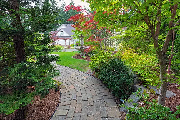 Garden brick paver path in frontyard with water fountain plants shrubs evergreen and deciduous trees landscaping