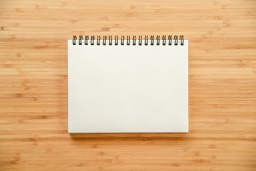 empty white paper page of binder notebook on wooden texture of office table - use for background in business or education concept