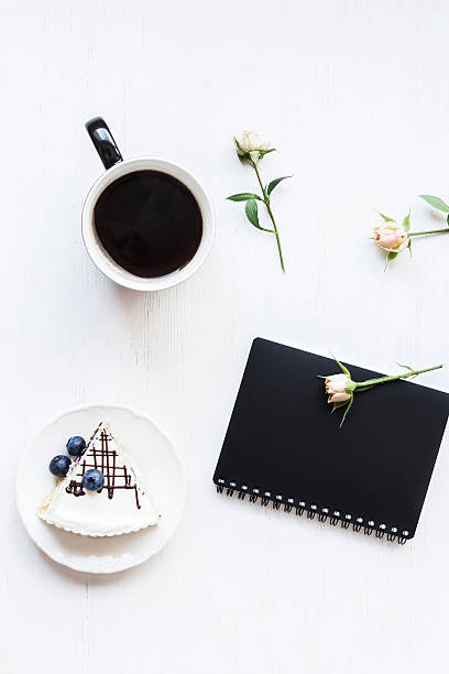 Workspace with notebook, cup of coffee, cake and rose flower