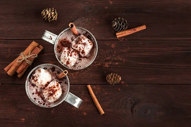 Hot chocolate in a mugs, marshmallows, cinnamon sticks and fir cones, top view, flat lay