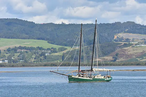 Two masted sailship with green hull in sheltered harbour.