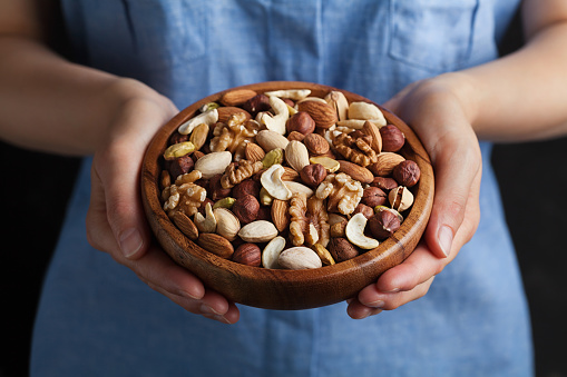 Womans hands holding a wooden bowl with mixed nuts. Healthy food and snack. Walnut, pistachios, almonds, hazelnuts and cashews.