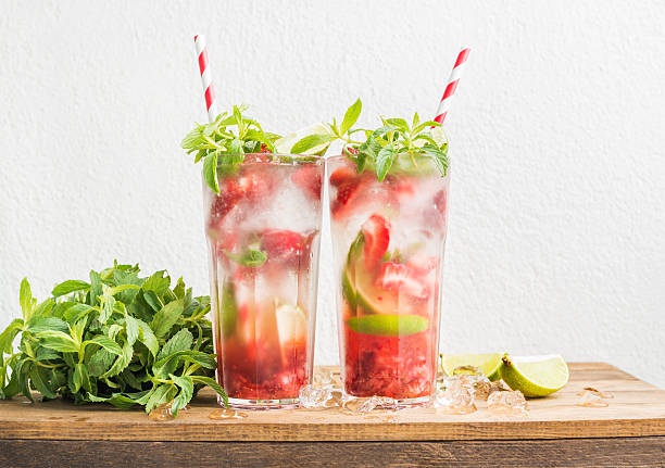 Strawberry mojito summer cocktails with mint and lime in tall glasses. White wall background