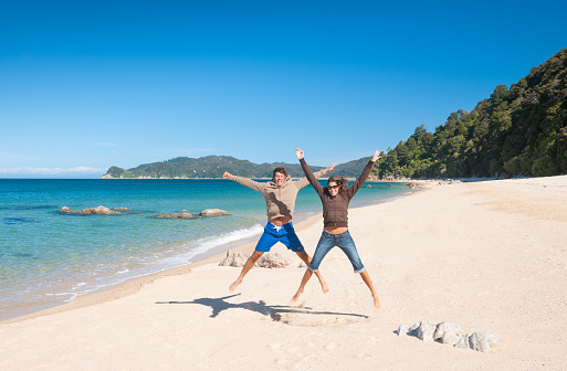 Tourist Couple jumping at the Beach. Abel Tasman National Park in New Zealand. 
