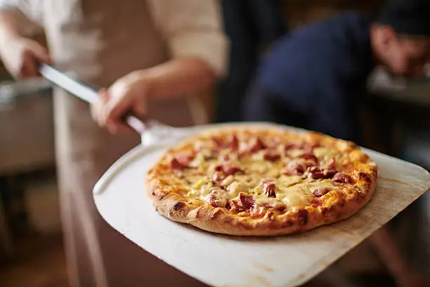 Traditional pizza being taken out of oven