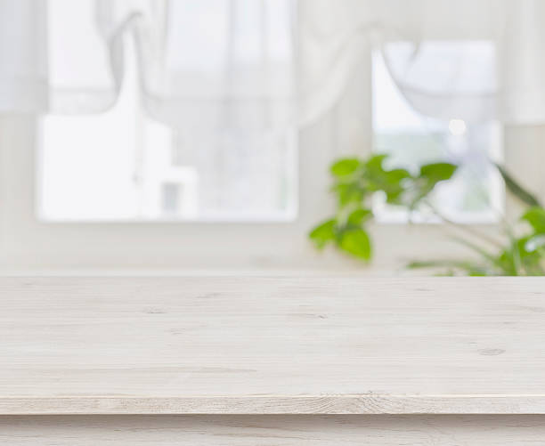 istock Wooden table over defocused green leaves and curtained window background 582303540