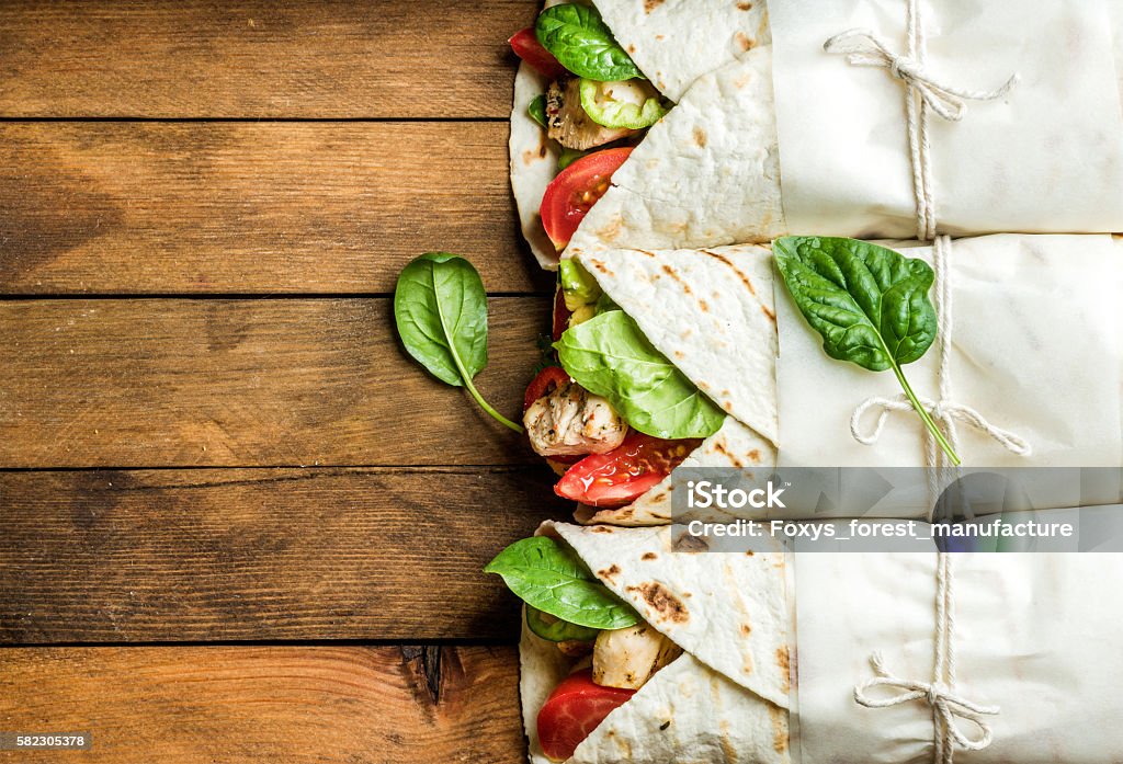 Healthy lunch snack. Tortilla wraps with grilled chicken fillet and Healthy lunch snack. Tortilla wraps with grilled chicken fillet and fresh vegetables on rustic wooden background. Top view, copy space Wrap Sandwich Stock Photo