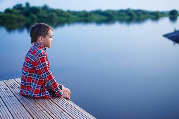istock boy at dusk sits on the docks and looks afar 582307880