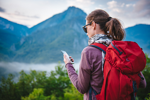 Woman with red backpack hiking on the mountain and using smart phone