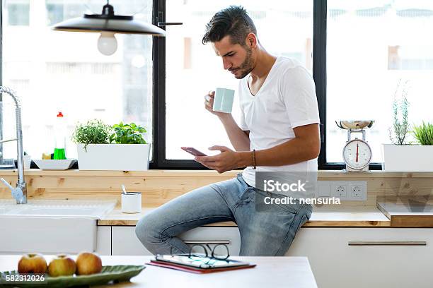 Hübscher Junger Mann Mit Seinem Handy In Der Küche Stockfoto und mehr Bilder von Männer