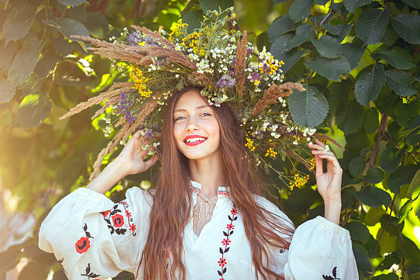Beautiful girl in meadow in national suite beautiful girl in wreath of flowers in meadow on sunny day. Portrait of Young beautiful woman wearing a wreath of wild flowers. Young pagan Slavic girl conduct ceremony on Midsummer. Earth Day slavic culture photos stock pictures, royalty-free photos & images
