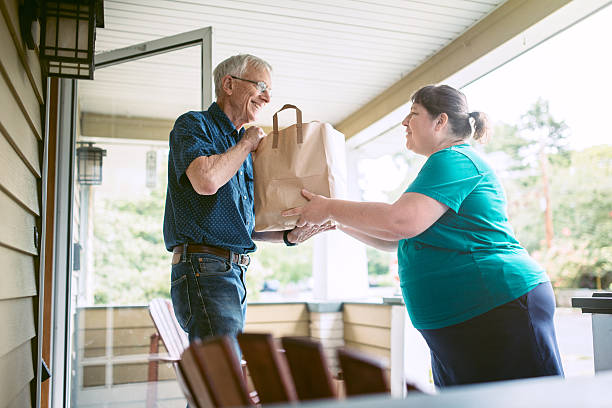 Delivering Groceries To Senior Man A kind and caring neighbor or friend delivers fresh produce from the grocery store to an elderly man at his home.  He receives the gift with a smile on his face, grateful for the help and assistance.  Horizontal image. doing a favor stock pictures, royalty-free photos & images