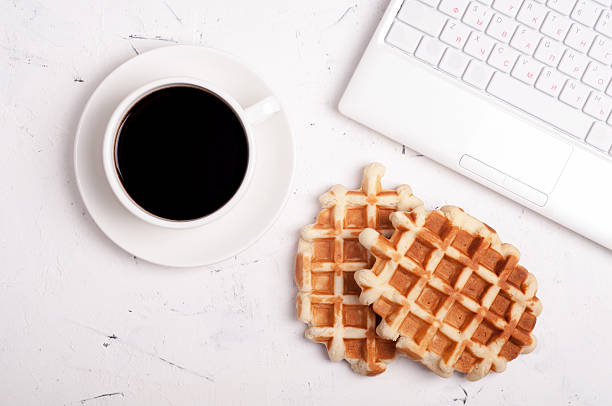 istock Coffee break concept. Desk table with laptop, coffee cup, waffles 582319682