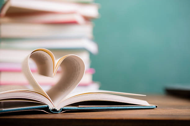 I love to read!  A heart shape created with open hardback book pages in foreground with a large stack of books and green chalkboard in background.  School classroom or library setting.  Education themes.   No people.
