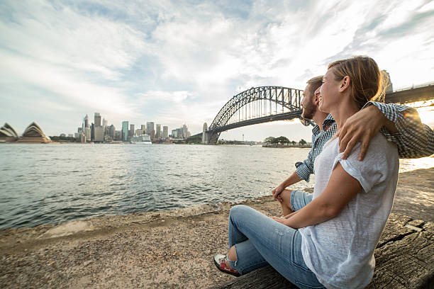 un couple caucasien regardant l’horizon de sydney au coucher du soleil - opera house sydney australia australia bay photos et images de collection