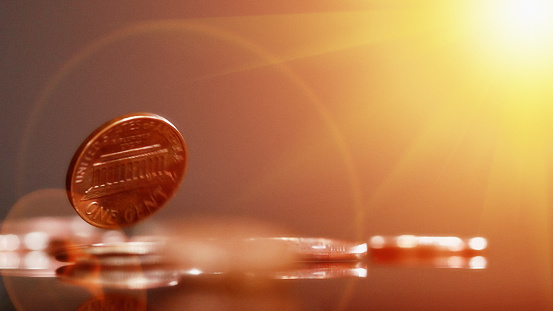 US one cent coin or penny falling onto other coins on a reflective surface, showing  motion blur and lens flare. Copy space on the gold-coloured background.