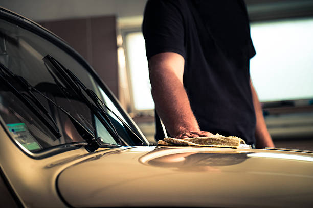 Adult man polishing oldtimer car in workshop with cleaning cloth stock photo