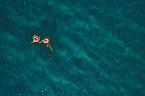 High angle view photo of a two young women relaxing, while floating in the ocean using swimming tubes