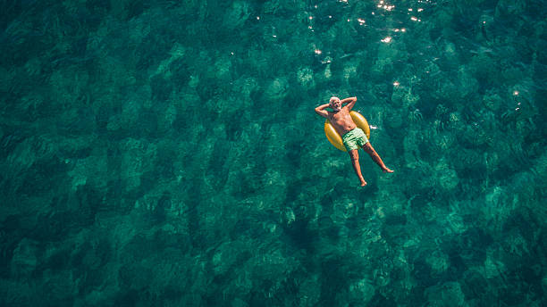 Relaxing in the sea High angle view photo of a senior man relaxing while floating in the ocean using swimming tube; wide photo dimensions floating on water stock pictures, royalty-free photos & images