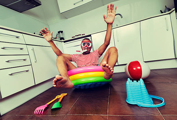 man swimming in an inflatable water pool, indoors young man wearing a diving mask and a snorkel pretending he is swimming into an inflatable water pool, placed in the kitchen, with a distortion effect staycation stock pictures, royalty-free photos & images