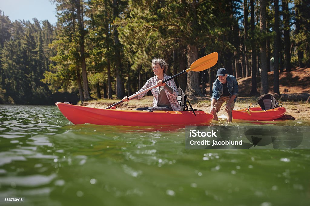 Mature couple having fun kayaking in the lake Portrait of mature woman canoeing in the lake with man about to catch the kayak from behind. Senior couple having fun kayaking in the lake. Kayak Stock Photo