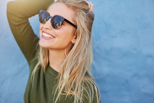 Cheerful young woman in sunglasses against blue background. Beautiful female model with long hair.