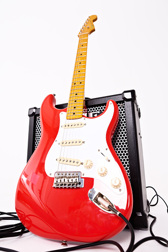 Cape Town, South Africa - July 2, 2016: A Stratocaster in the vintage Fender color Fiesta Red. This instrument is part of the Classic Vibe series manufactured in China by the Fender subsidiary Squier in 2013. The Classic Vibe guitars have been acclaimed by reviewers and guitarists around the world for their superior quality at comparatively affordable prices, although they are more expensive than other Squiers. This model reproduces vintage features of Fender Strats made in the 1950s. It is leaning against a Roland Cube 80GX amplifier and shot from a low angle distorting its shape..