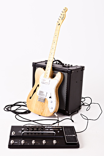 Cape Town, South Africa - July 2, 2016: A Telecaster Thinline electric guitar manufactured by Squier, a budget brand owned by the Fender Musical Instrument Corporation. This instrument is part of Squier's Vintage Modified series, a line introduced in the 2000s to good reviews for its price:performance ratio. This example was made in Indonesia in 2014, and is an authorized reproduction of the semi-hollow Fender Telecaster Thinline model introduced in 1972, sporting humbucking pickups, a novelty for Fender at the time. The guitar is leaning against a Roland Cube 80GX amplifier, with a defocused multi-effects unit in the foreground.