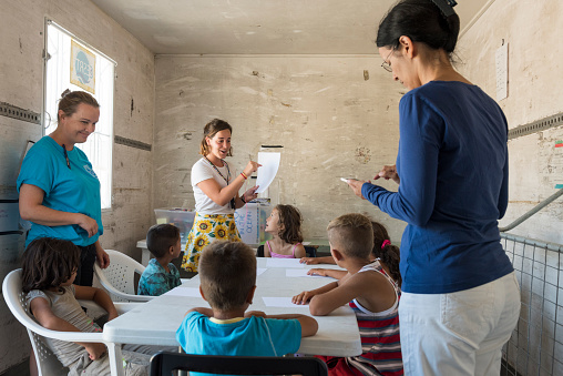 Chios, Greece - July 27, 2016: NGO Drop in the Ocean volunteers (teachers) have arranged an improvised school for refugee children with a classroom in a container. They are offering English lessons. The image was captured through the open door of the container just outside the Souda refugee camp in Chios Town on the Greek Island of Chios in the Aegean Sea at midday on a hot summer day.