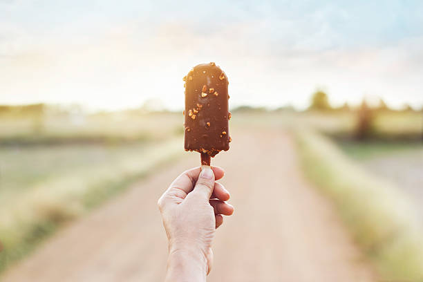 рука женщины, держащей шоколадное эскимо на фоне природы - people snack almond brown стоковые фото и изображения