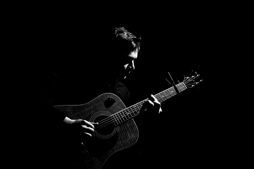 Male musician playing on acoustic guitar. Black and white photo.