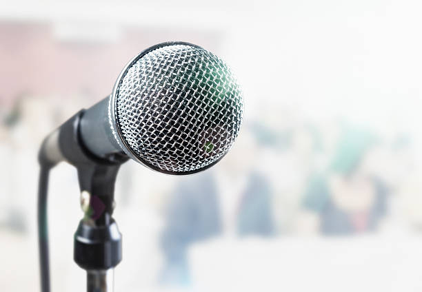 istock Close up of microphone with defocused seated audience 583800946