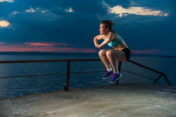 Young caucasian woman in sportswear doing plyometric exercises on pier. Fitness workout outdoors