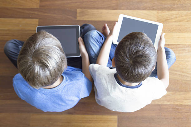 istock Children using tablets PC sitting on wooden floor at home 583802166