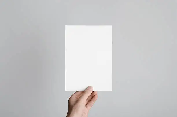 Male hands holding a blank flyer on a gray background.