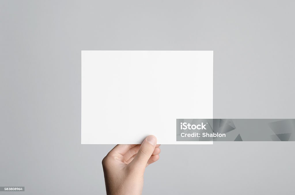 A5 Flyer / Postcard / Invitation Mock-Up Male hands holding a blank flyer on a gray background. Postcard Stock Photo