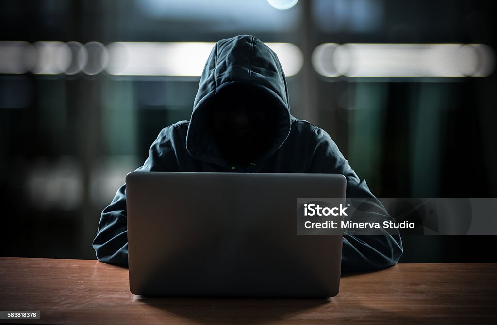 Hacker in front of his computer Hacker in front of his computer. Dark face Computer Hacker Stock Photo