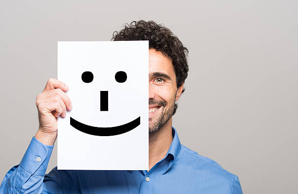 istock Man covering half his face with a smiling emoticon 583820260