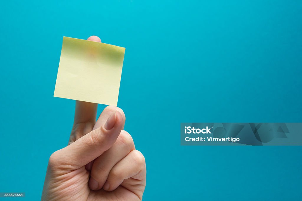 Sticky note, finger up of thumb, yellow reminder on blue Hand holding yellow note reminder on finger with copy space for ad on blue background Reminder Stock Photo
