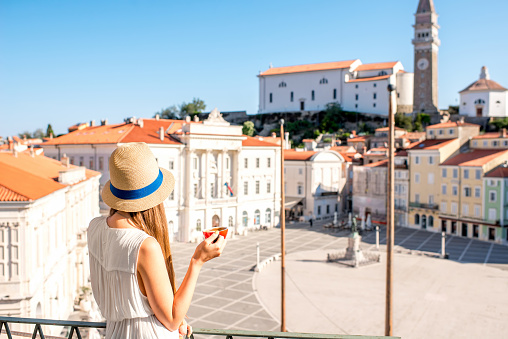 Young female traveler using mobile phone sitting on the central square in Piran old town. Traveling in Slovenia