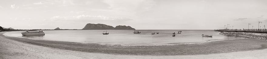 panorama view of sea and beach with traditional boat, bridge, long mountain in background, black and white, brown vintage picture style. Grain added
